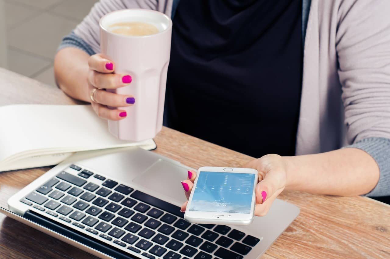 using an iPhone and laptop while having a coffee